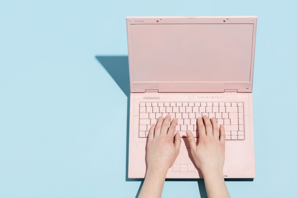 Woman's hands typing on a pastel pink keyboard of retro laptop. Work and technology.