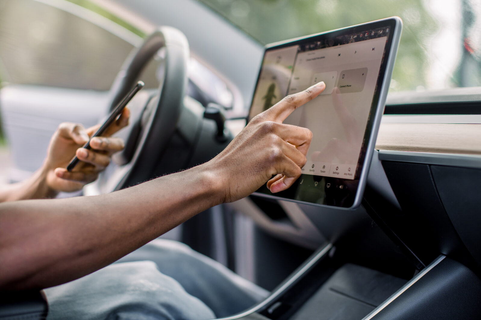 Autopilot self-driving car system with no human intervention. Close up cropped image of hand of African male driver browsing the internet using smartphone and touchscreen in futuristic autonomous car