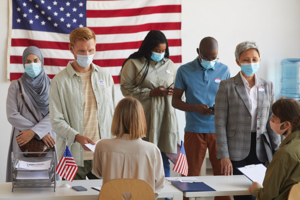 Multi-ethnic group of people standing in row and wearing masks at polling station on election day