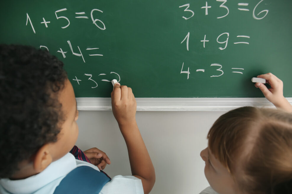 Schoolchildren writing on chalkboard in classroom during math lesson