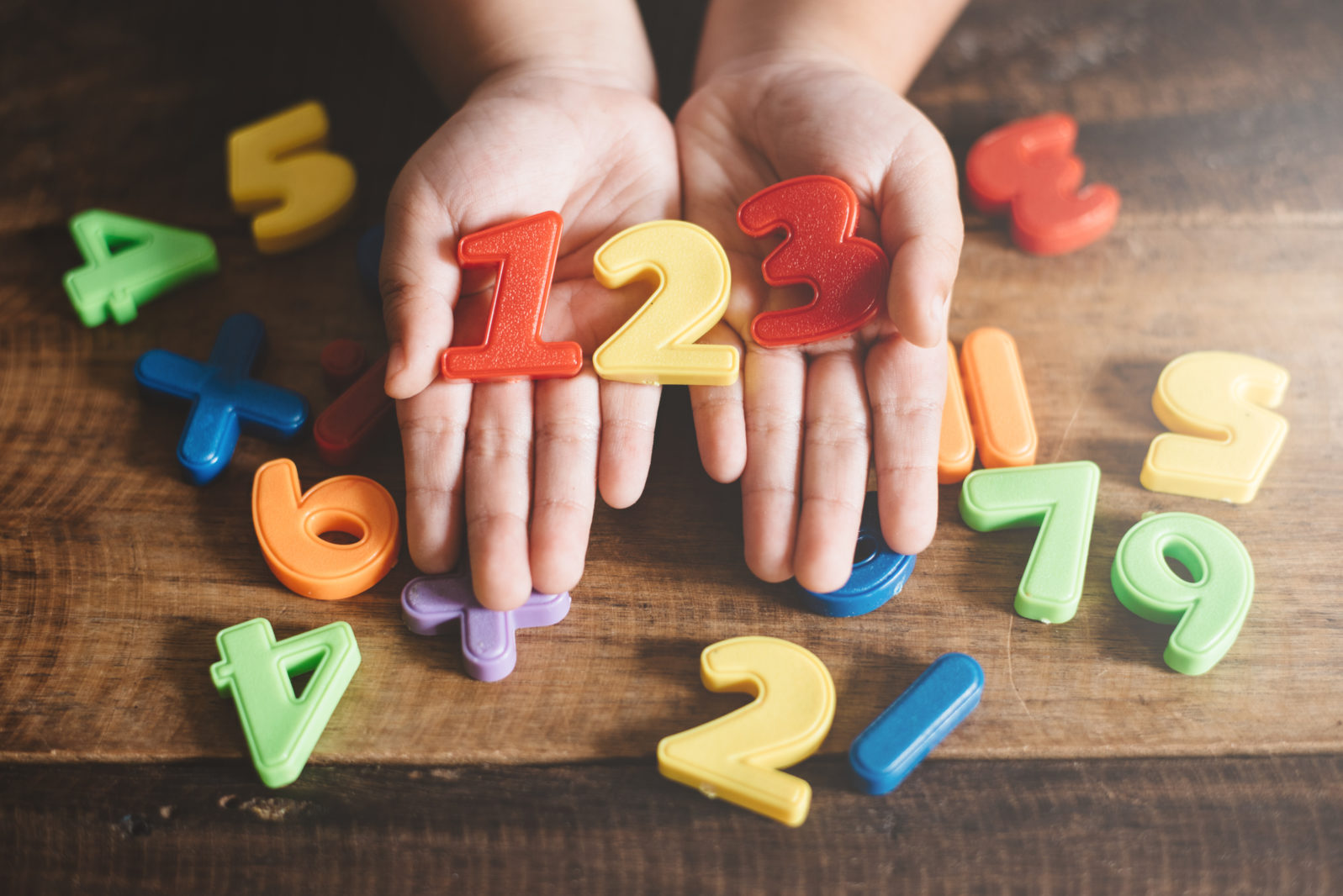child hands showing a colorful 123 numbers agains wooden table. Concept of Child education, learning mathematics and counting