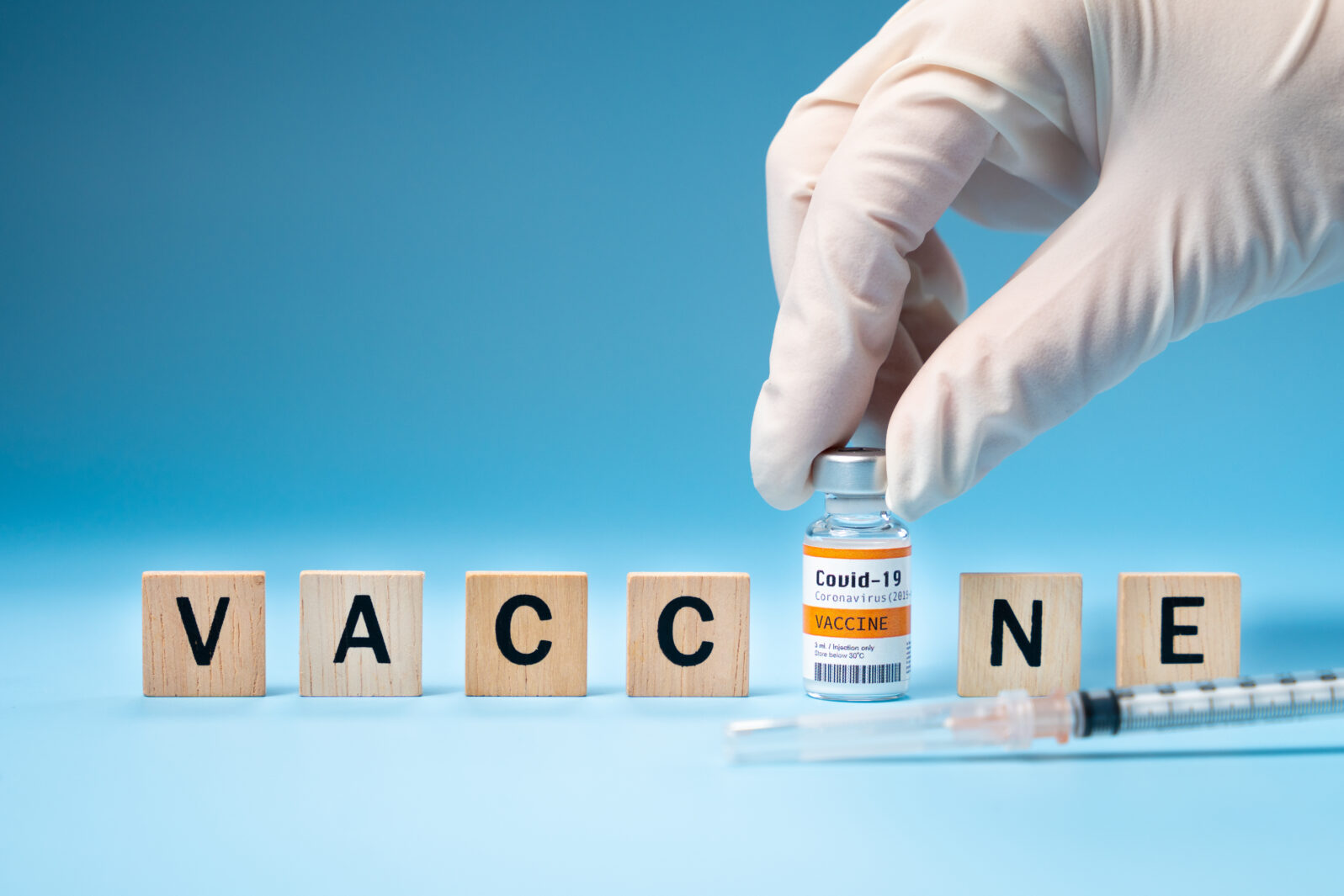 Promising Covid-19 Vaccine concept. Hand of a researcher take a 2019-nCov vaccine vial with wooden alphabet letters "VACCINE". Candidates, Authorized, Volunteers, Global trial, Hope, Successful.