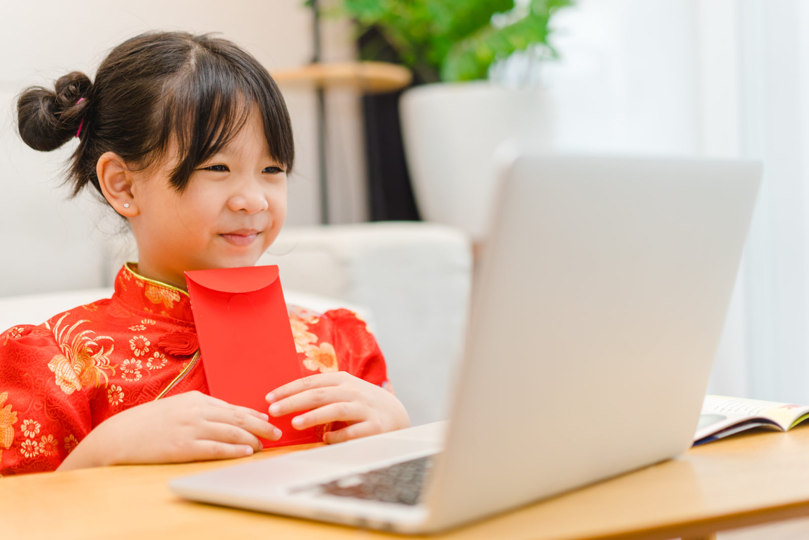 Happy chinese new year.Asian kid girl receive money online wearing chinese traditional qipao dress showing red envelope at home.Online party.Happy chinese new year covid19 lockdown.stay home holiday.