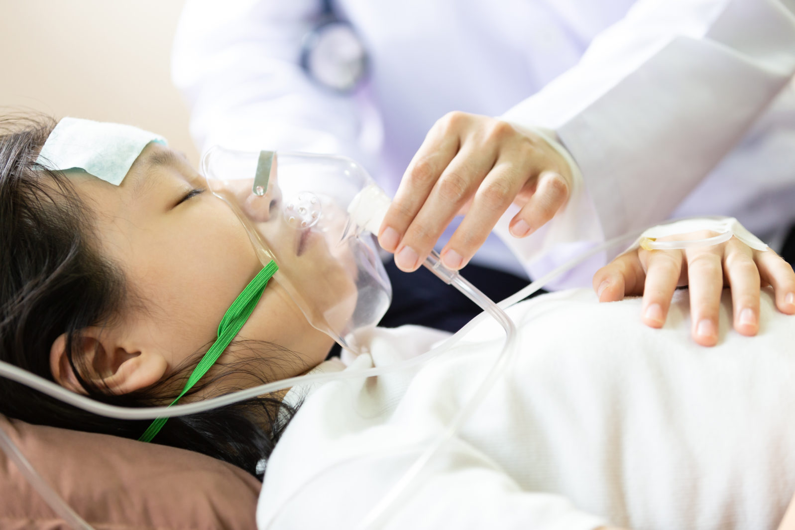 Closeup of hand female caregiver holding oxygen mask with cute child patient in hospital bed or home,little girl putting inhalation,doctor or nurse intensive care,health care,support,help concept