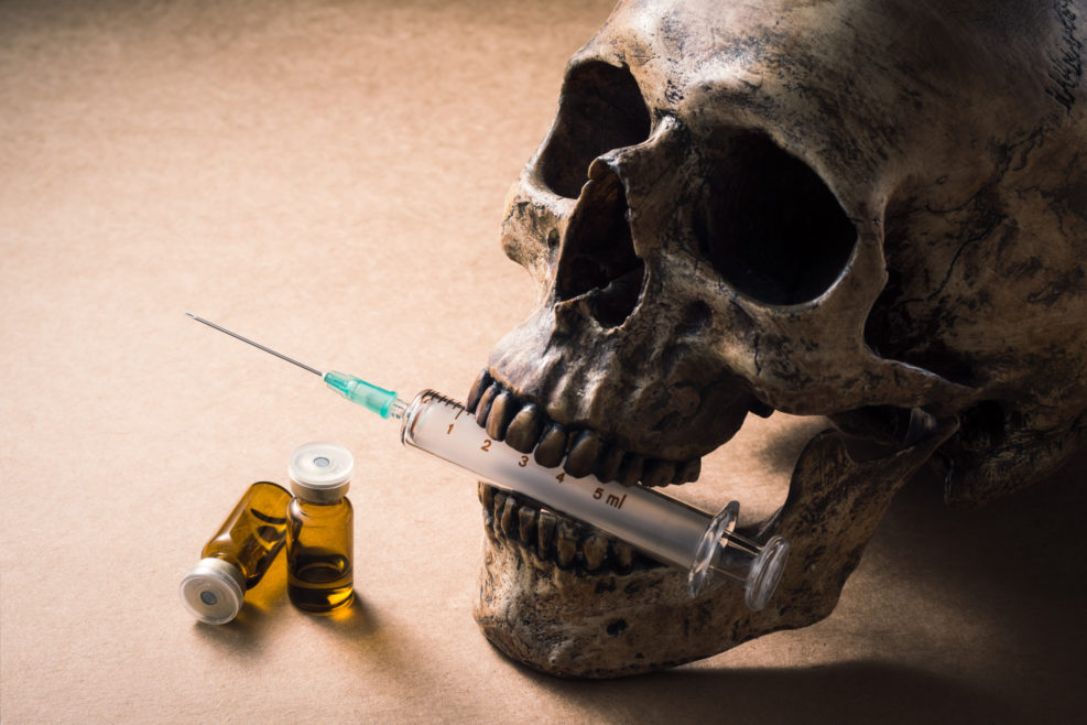Human skull with a syringe holds in the mouth and vaccine bottle on space of brown paper, Bad side effect concept
