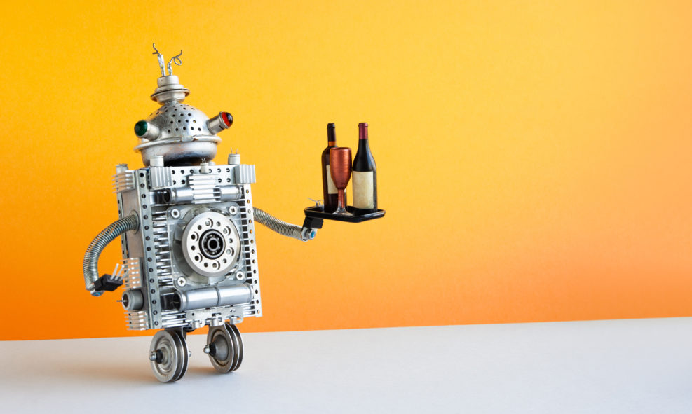 Restaurant automation service concept. Robot waiter serving a tray with a bottles and wine glass. Two wheels robotic character on yellow wall, gray floor background. copy space
