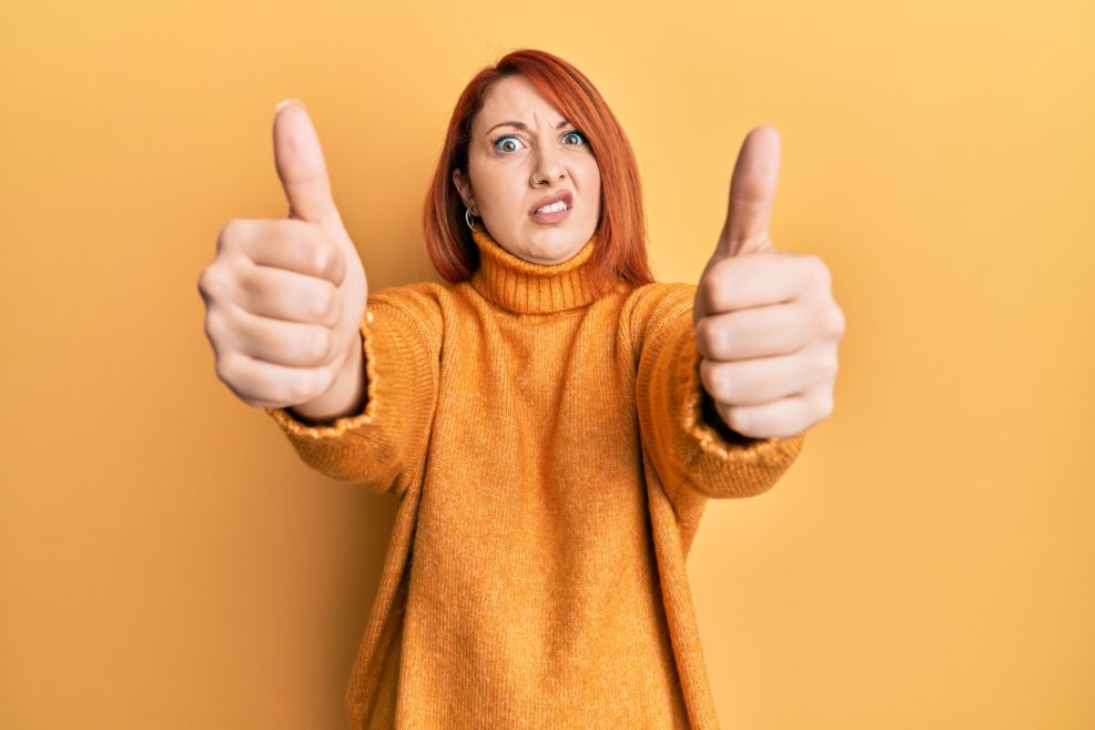 woman doing thumbs up positive gesture in shock face, looking skeptical and sarcastic, surprised with open mouth