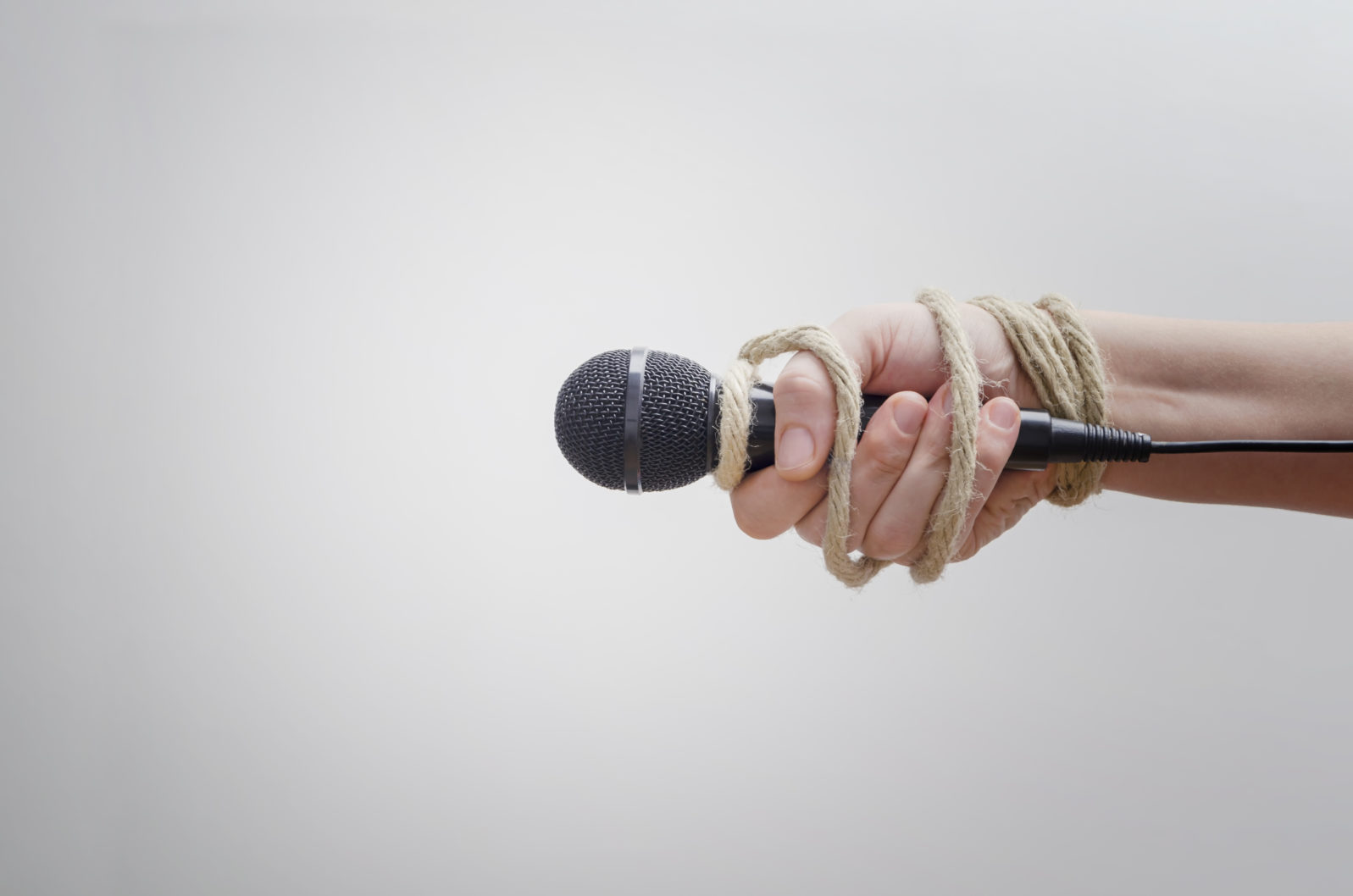 Hand with microphone tied with rope, depicting the idea of freedom of the press, idea of the repression of the mass media or freedom of expression