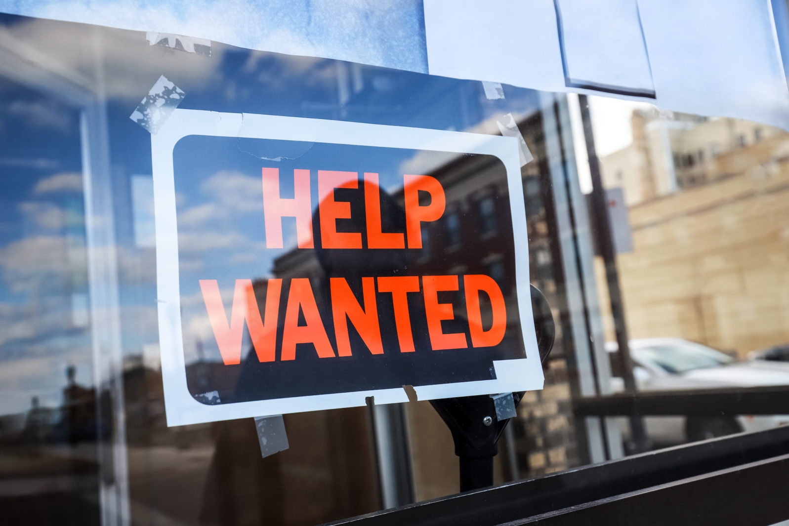 Reflection of a man looking at a help wanted sign in a business window, economy concept