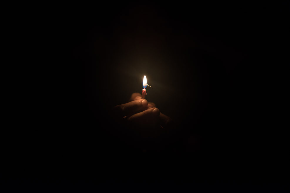 Hand holding burning candle in the dark