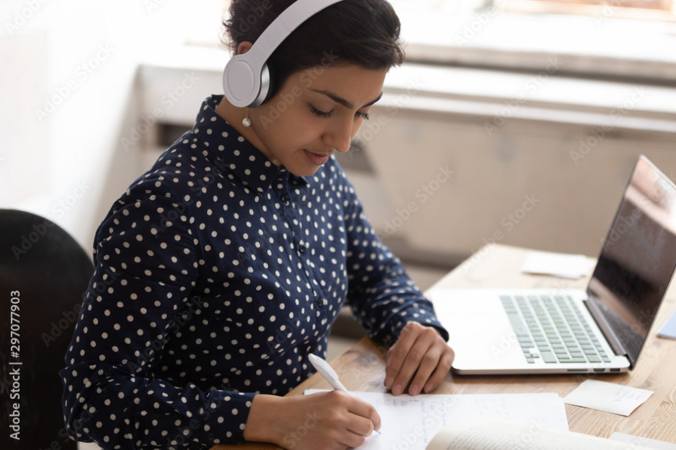 Indian ethnicity woman wearing headphones listens educational course studying online