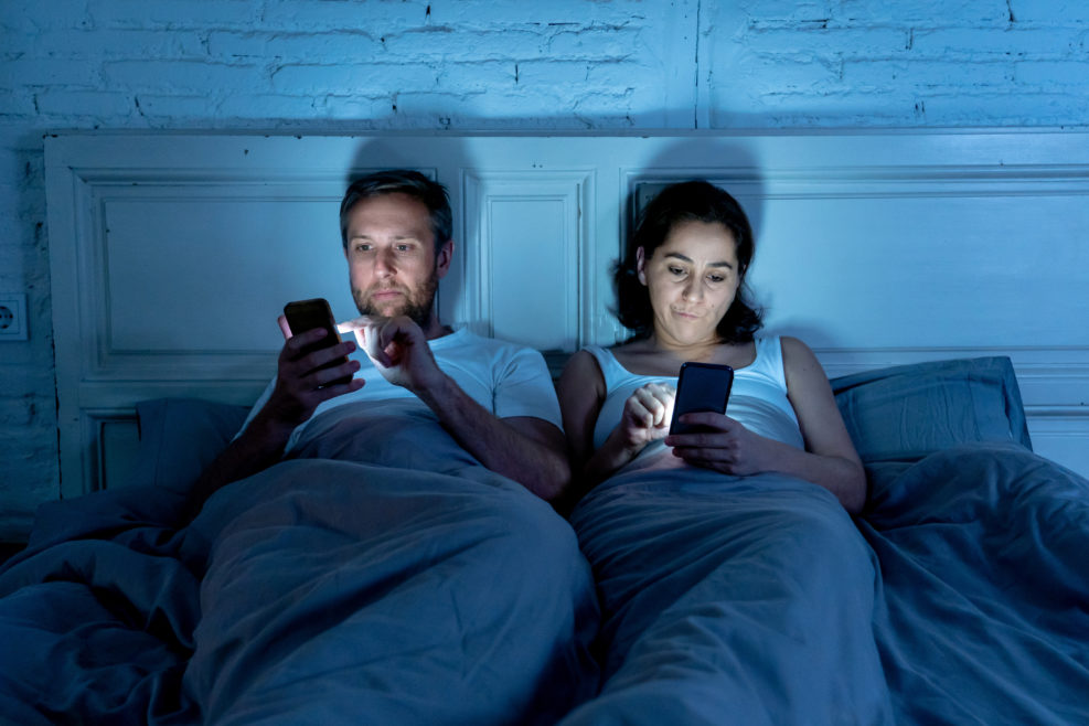 Couple in bed on mobile phones ignoring each other in relationship problems and technology addiction