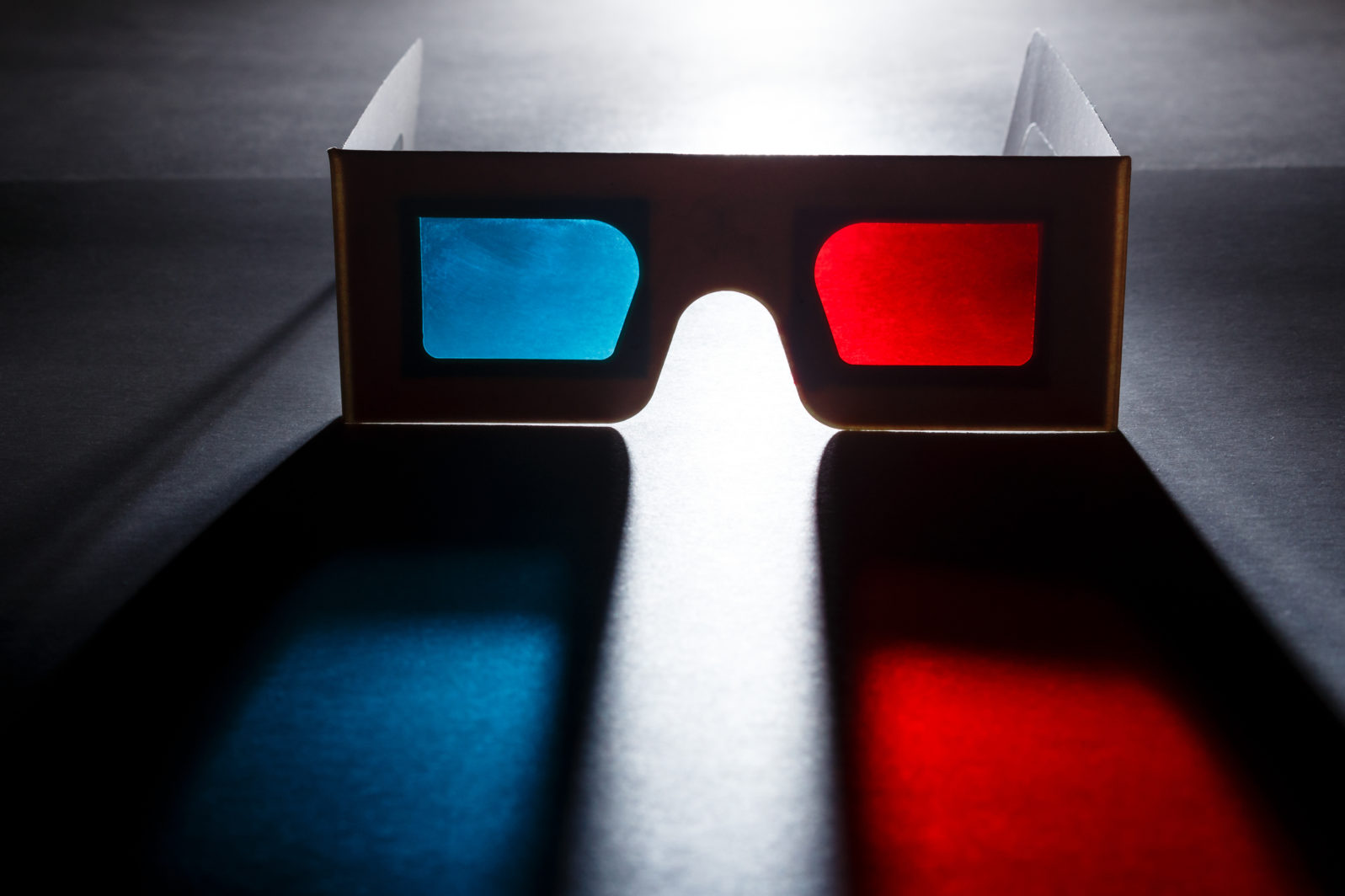 Movie at cinema concept. 3D glasses with red and blue lenses with soft colored shadow on dark background.