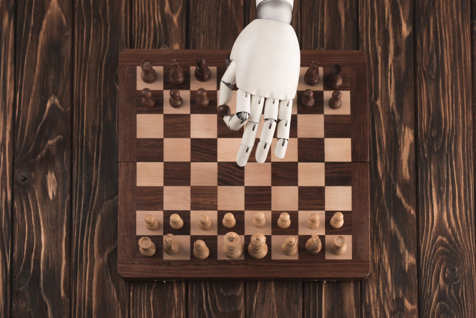 cropped shot of robot playing chess on wooden surface