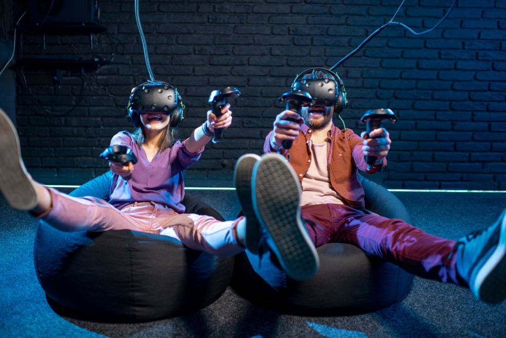 Man and woman shooting with gamepads while playing in virtual reality using VR headsets in the playing room