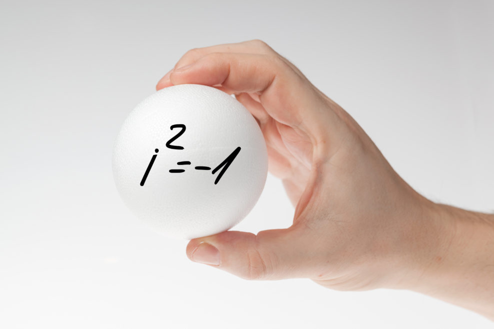 Man's hand holding white blank styrofoam ball with handwritten imaginary number formula against the white background.