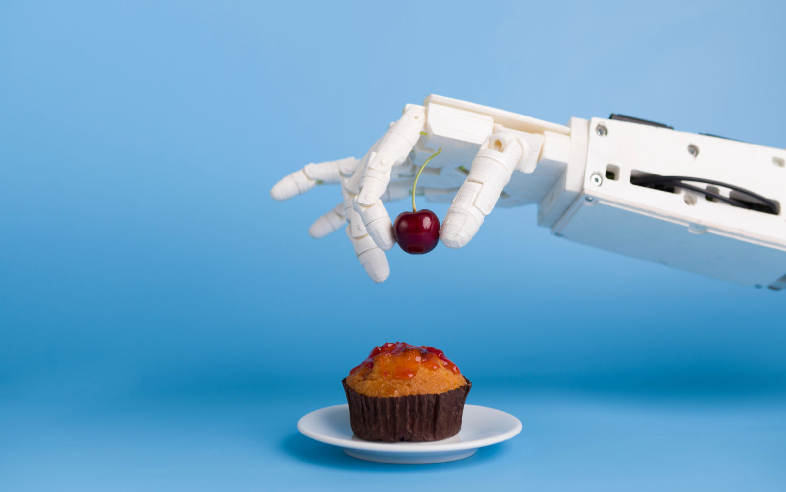 Robot hand putting fresh cherry on top of the cupcake