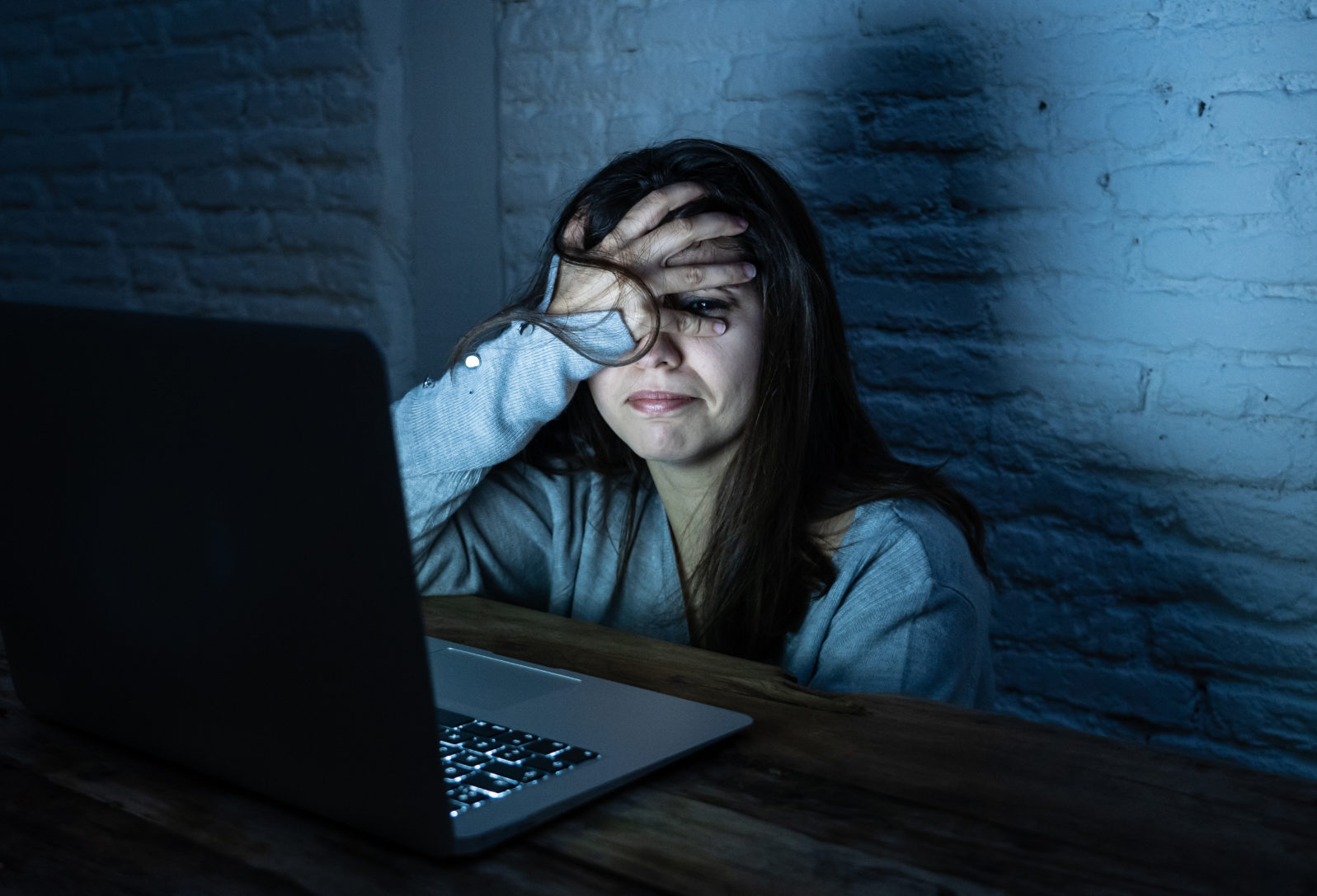 Scared woman on laptop in the dark feeling fear suffering online harassment and cyberbullying