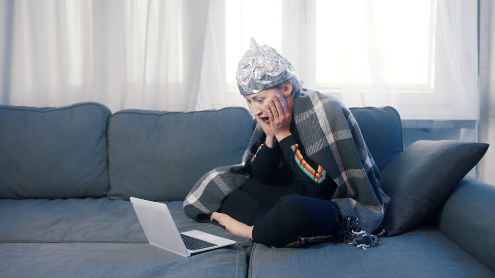 Fearful young woman with aluminum hat browsing social media. Conspiracy theory about 5g network destroying brain. High quality photo