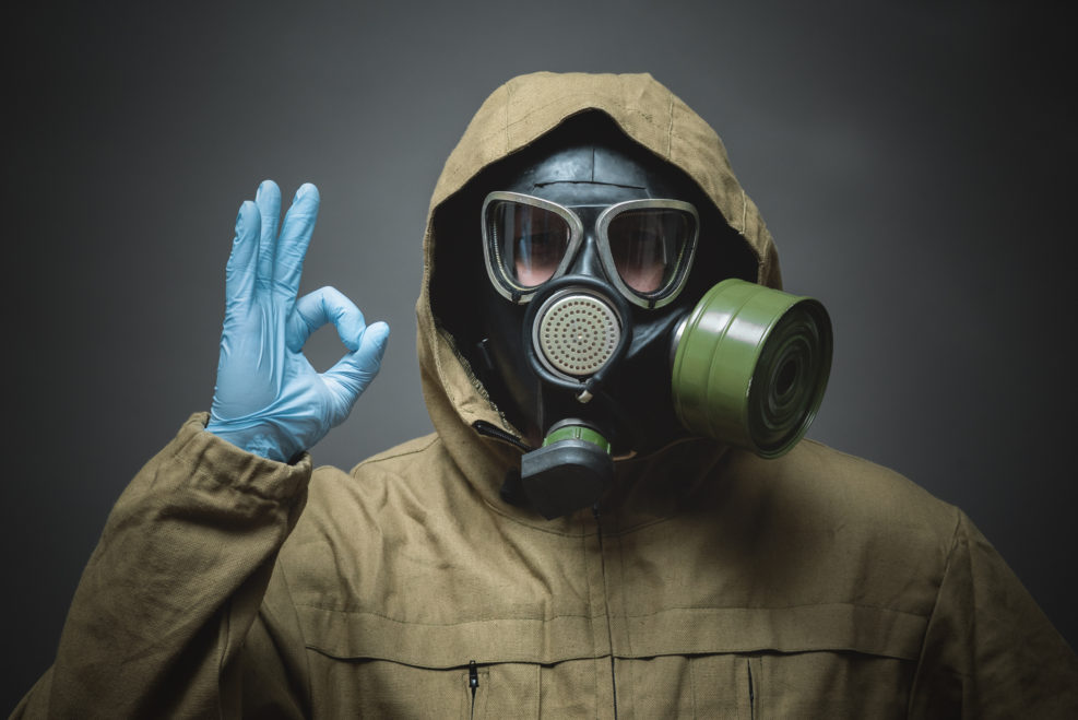 Man in gas mask is showing an Ok gesture by his hand close up on gray background.