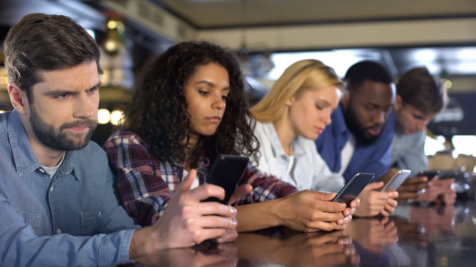 Multi-racial friends scrolling smartphones ignoring each other, gadget addiction