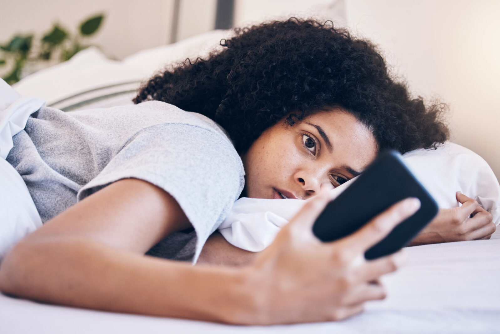 Cellphone, mental health and woman in her bed with depression while watching videos on social media. Tired, sleepy and depressed female with insomnia networking on a phone in her bedroom at home.