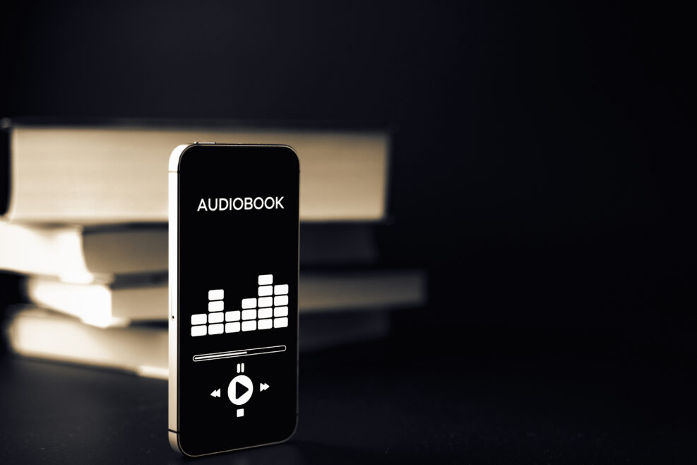 Audiobook education. Smartphone screen with audiobook application on paper books black background. Ebook e learning electronic internet mobility concept.