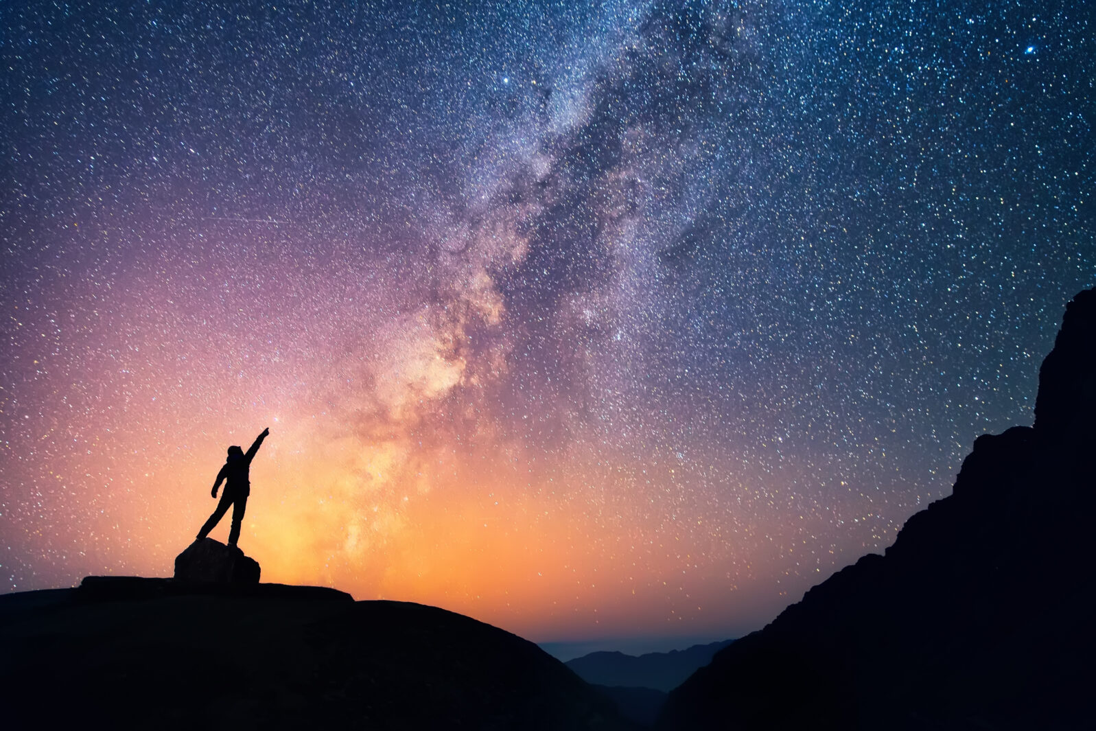 Catch the star. A person is standing next to the Milky Way galaxy pointing on a bright star.