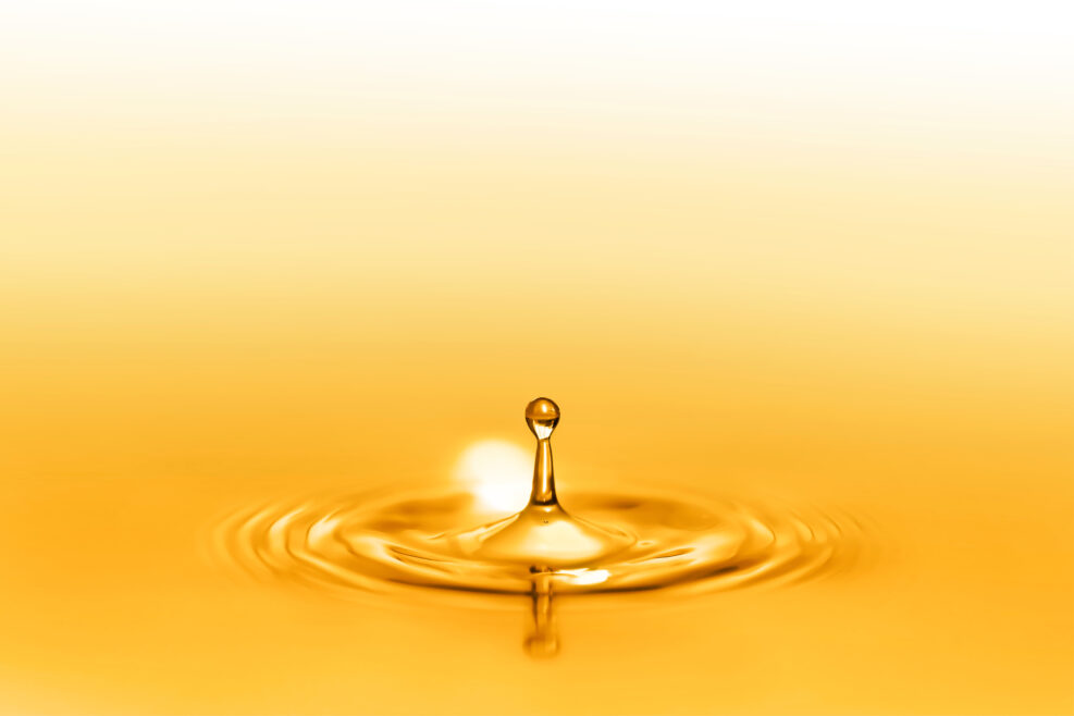 Close up on drop splash of a healthy extra-virgin oil full of oligo elements and vitamins creating circular waves by falling down on the liquid and seamless pure surface shining with golden reflects.