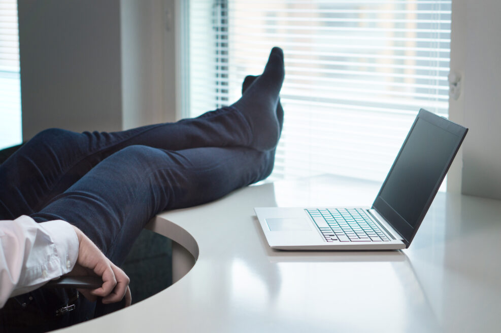 Lazy office worker with feet and socks on table. Useless and relaxing man doing nothing or taking break from work in workstation. Businessman resting during workday. Laziness and relax concept.