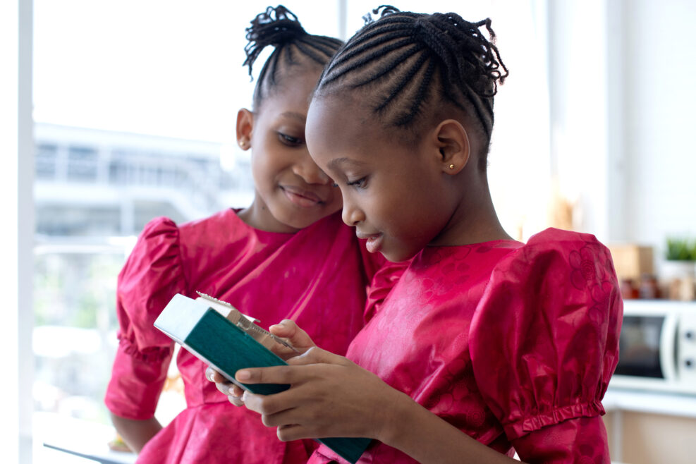 Twin African girls are interested and playing Kalimba or Thumb Piano acoustic music instrument from Africa, twins little African girls with her braided hair, African hair style