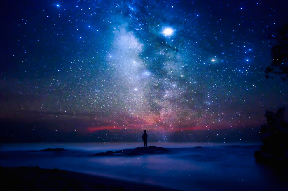 Starry night sky over sea and beach with man silhouette. man standing on sea beach under starry sky.