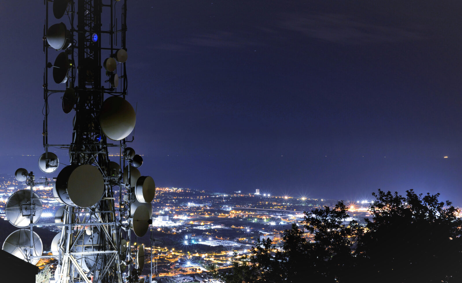 Telecommunications tower, antenna and satellite dish and city at night as background