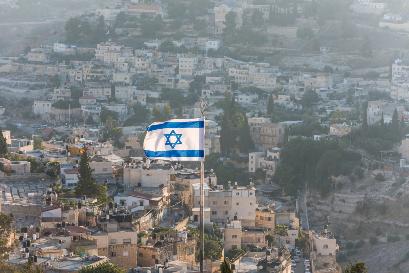 Israeli National flag waving on the top of Mount of Olive with background of residential houses in Jerusalem, Israel