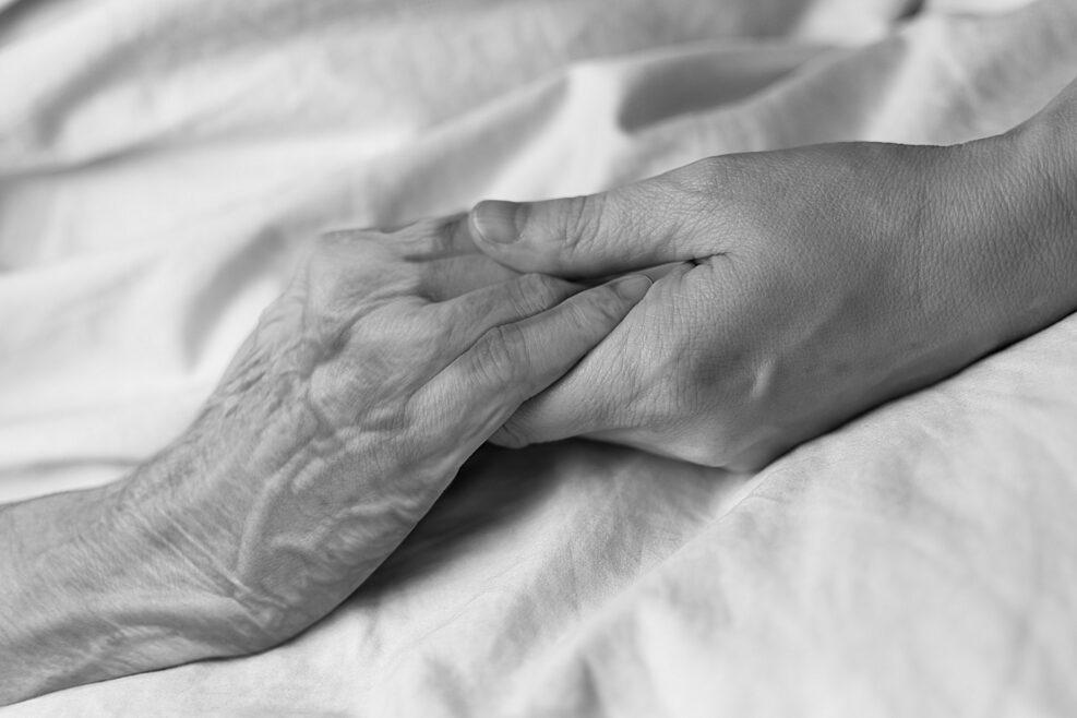 A young woman holding the hand of an old woman in a hospital bed, black and white