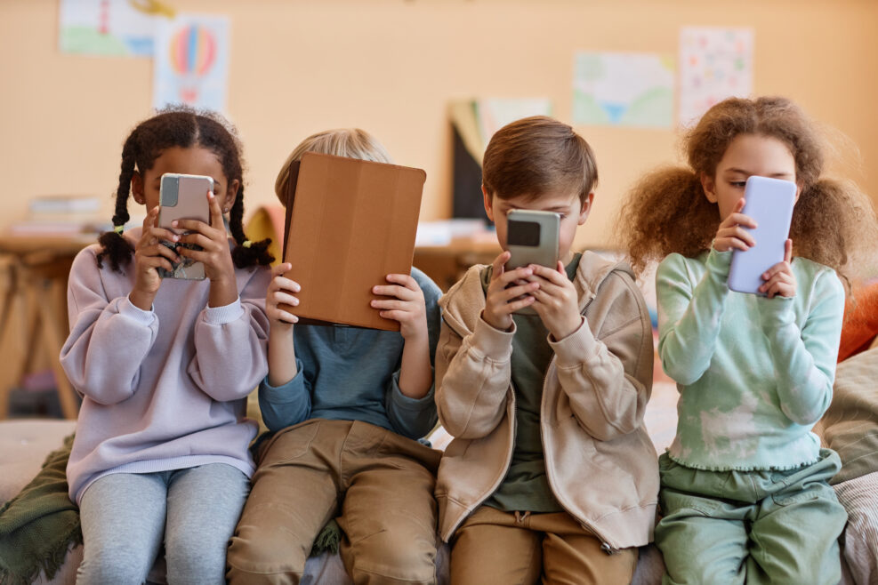 Group of young children holding smartphones and hiding faces, gen Alpha