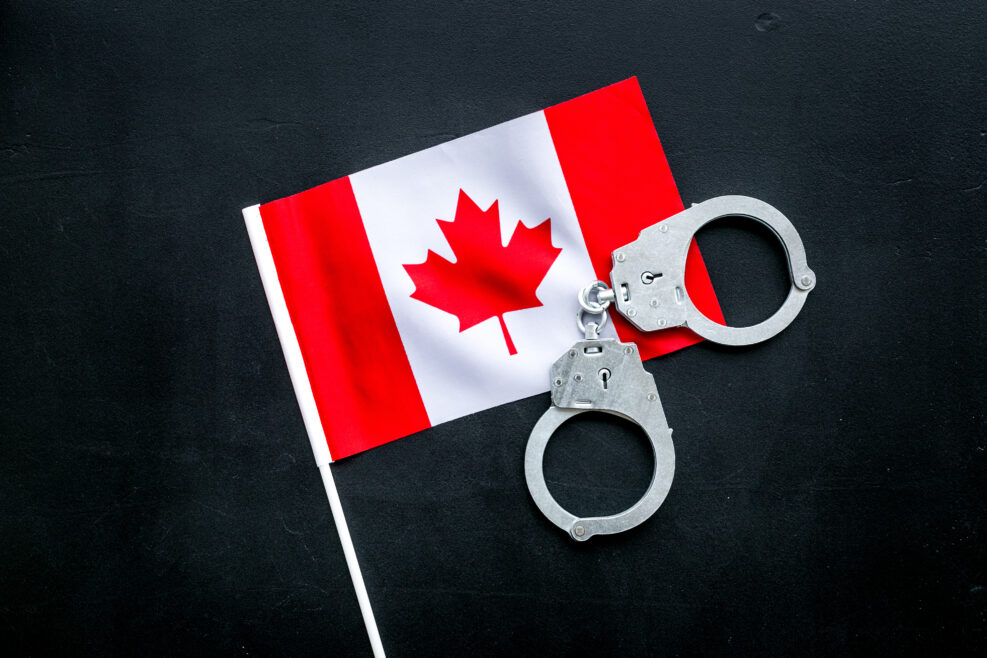 Violation of law, law-breaking concept. Metal handcuffs on Canadian flag on black background top view