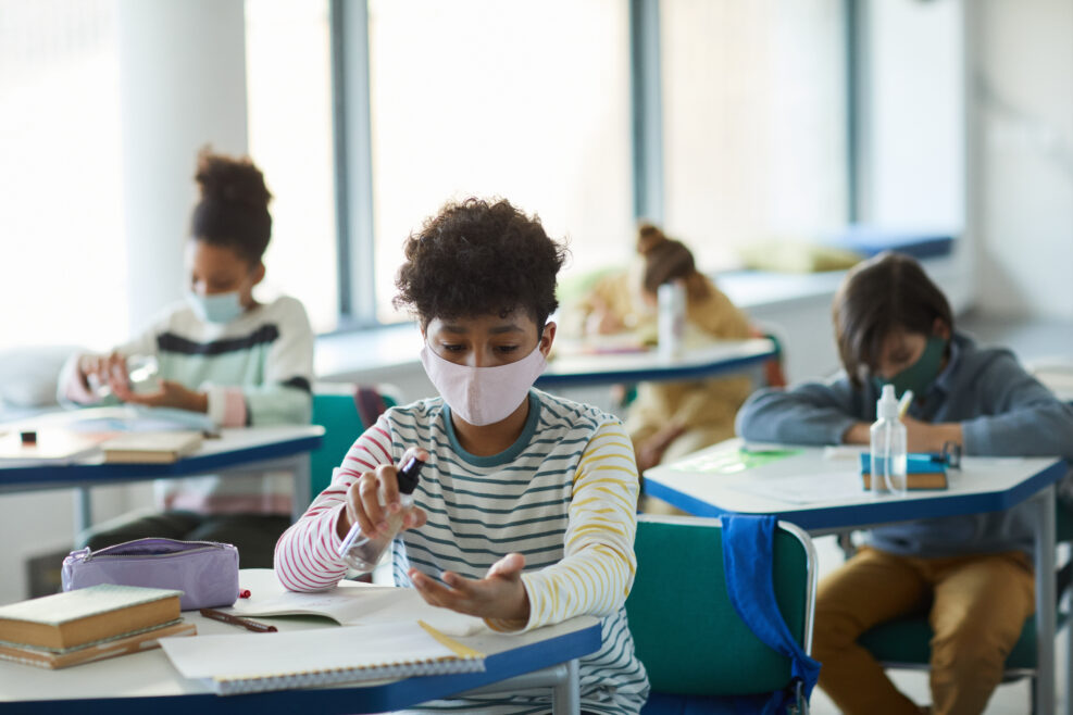 Portrait of young African-American boy sanitizing hands in school classroom, covid safety measures, copy space