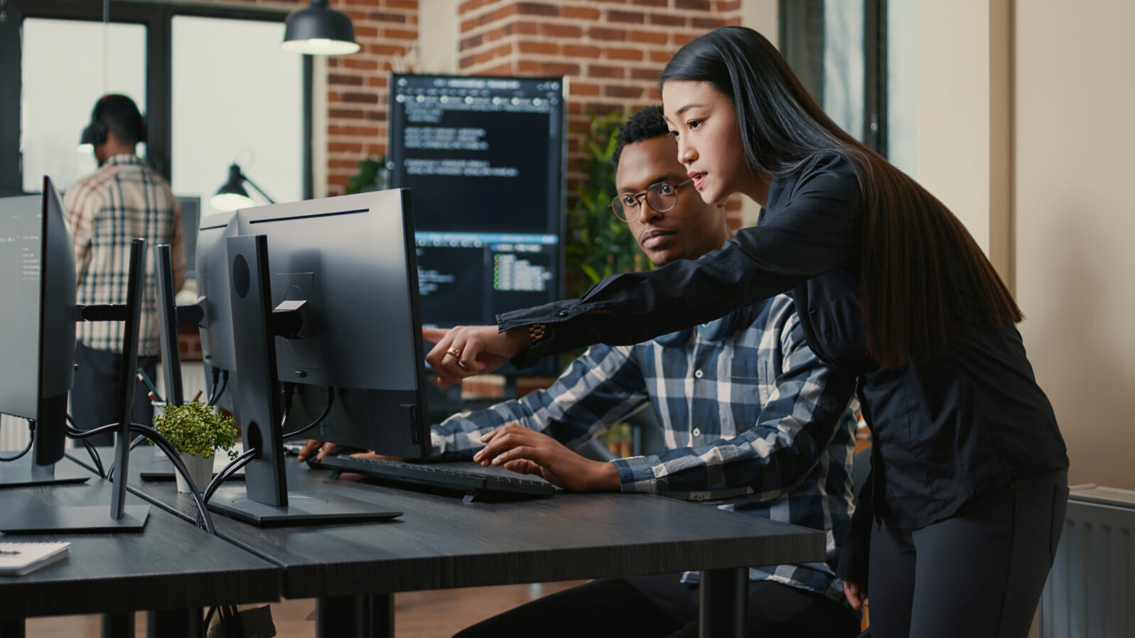 Two programers holding laptop with coding interface walking towards desk and sitting down talking about online cloud computing. Software developers team discussing algorithms on computer screen.