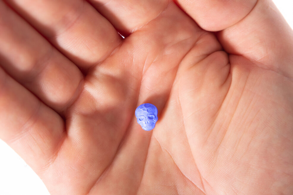 Top view of a caucasian hand with one blue MDMA, Amphetamine, Army Skull, Ecstasy, XTC pill.