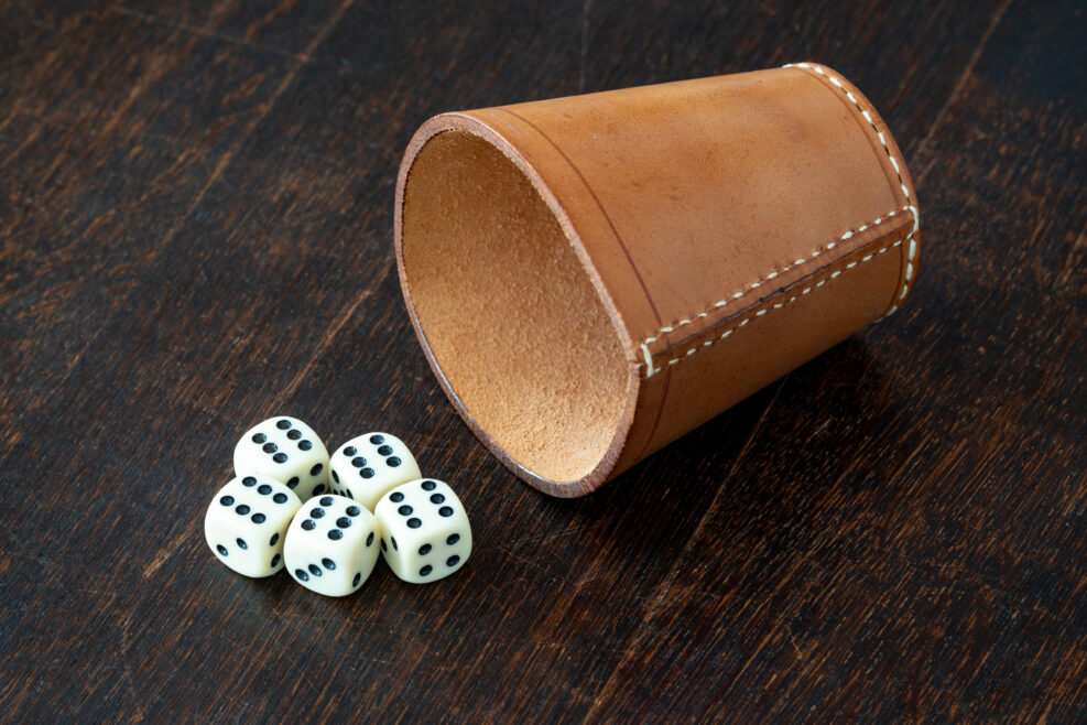 Leather dice cup and dice on the table, rolling all sixes with 5 dice representing gambling and luck