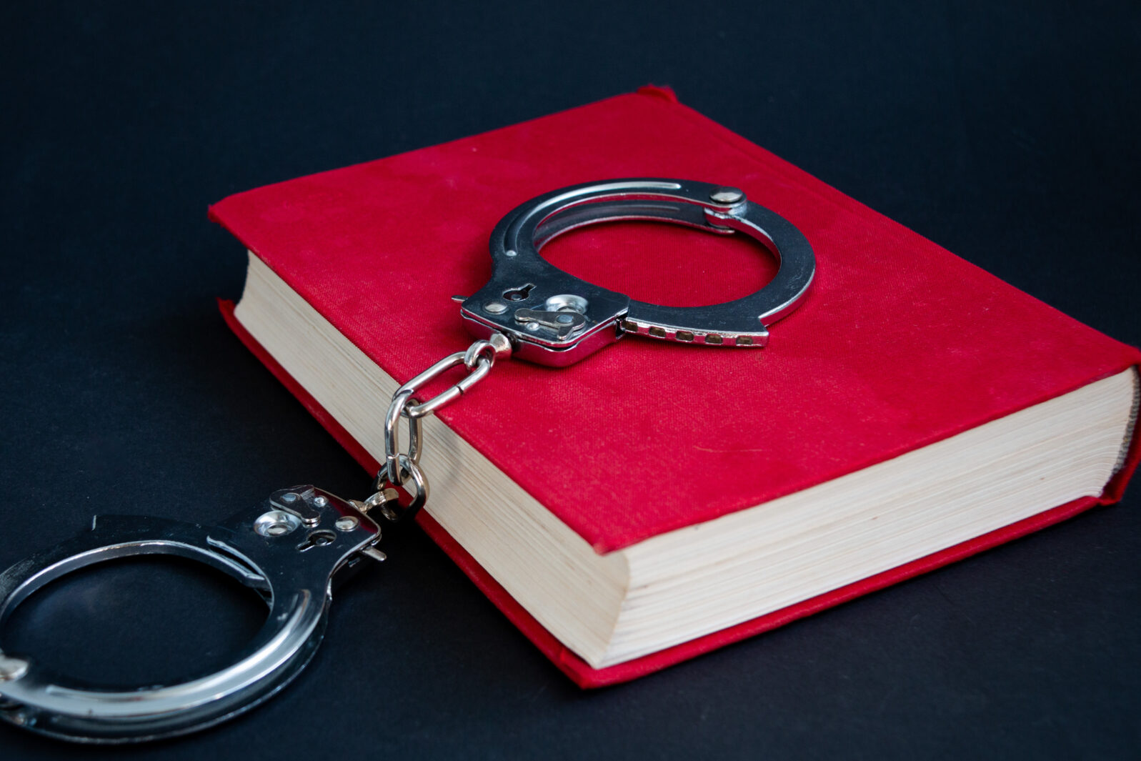 handcuffs on the red book of laws. close-up. Black background.