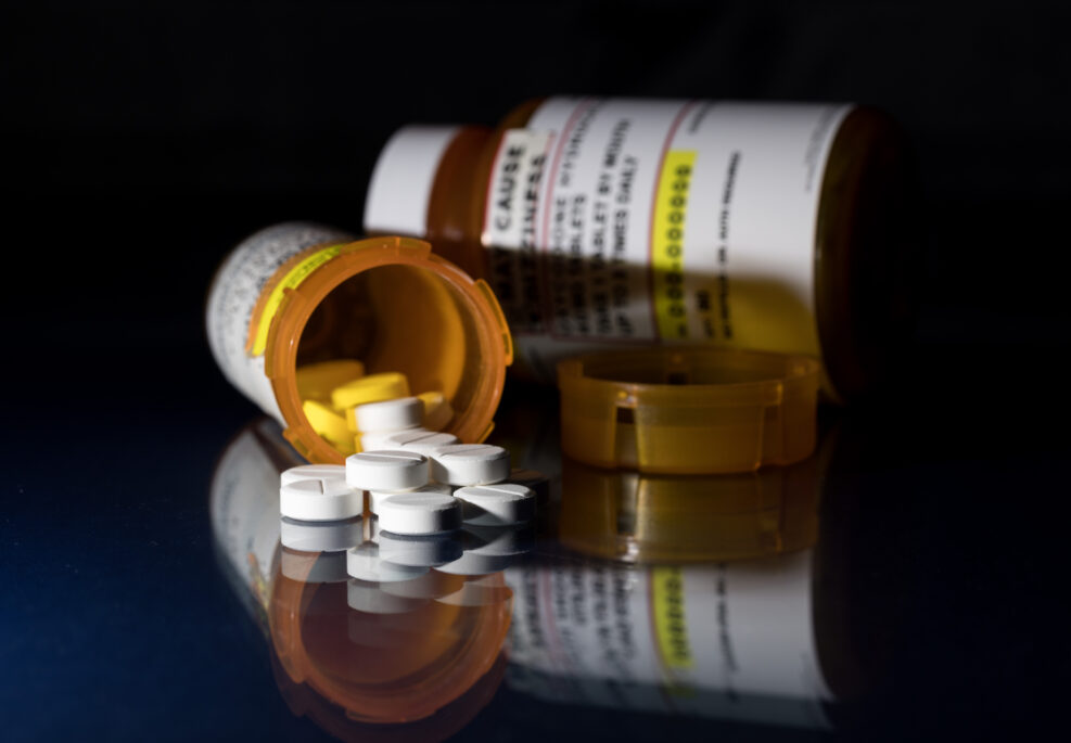 Oxycodone is the generic name for a range of opoid pain killing tablets. Prescription bottle for Oxycodone tablets and pills on glass table with reflections