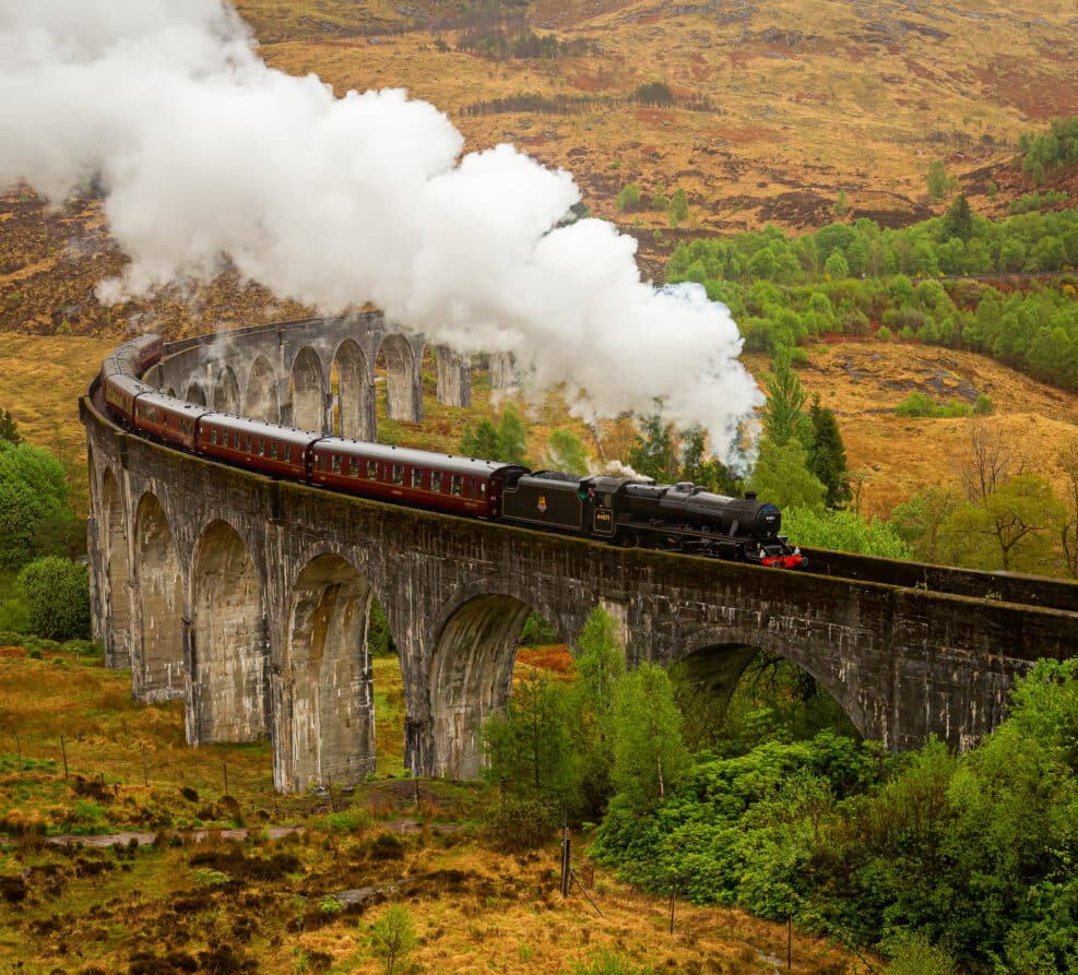 A Jacobite steam train travels over the Glenfinnan viaduct located in the Scottish Highlands. It is famous for being a location on the Harry Potter films as the Hogwarts Express.