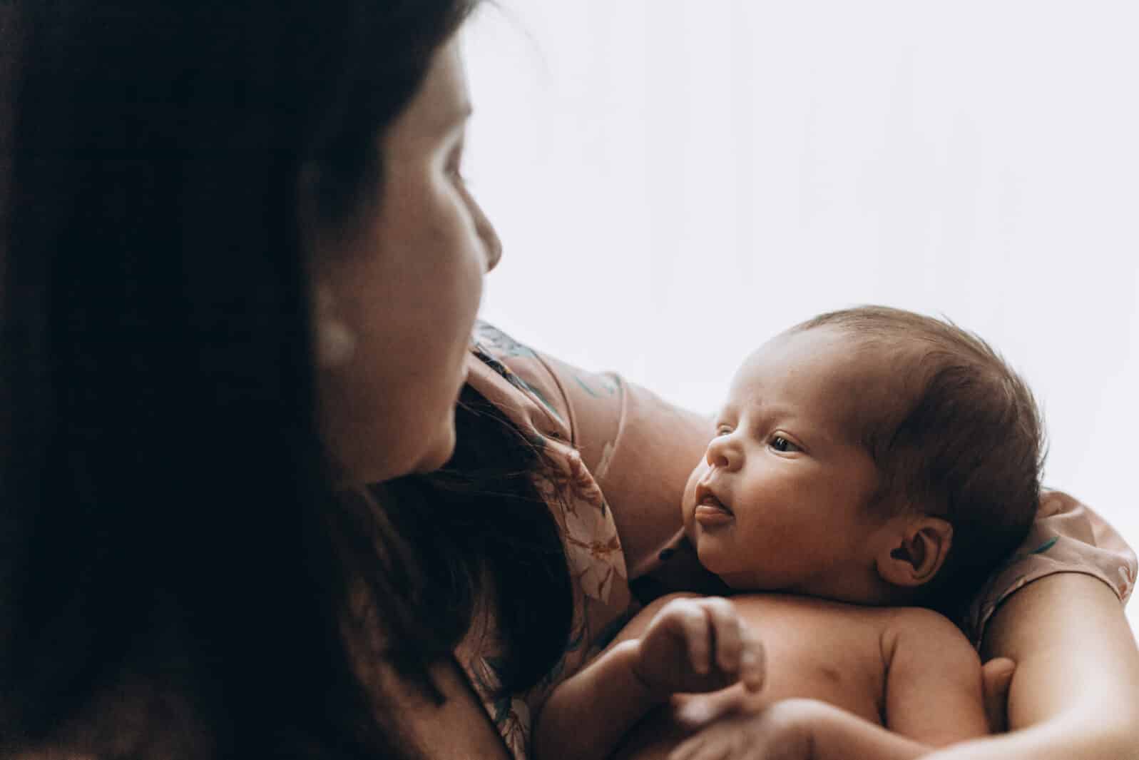 Happy Mothers day! Stylish Mother holding and hugging cute newborn baby in window light, close up. Motherhood and parenthood. Adoption and fertility concept