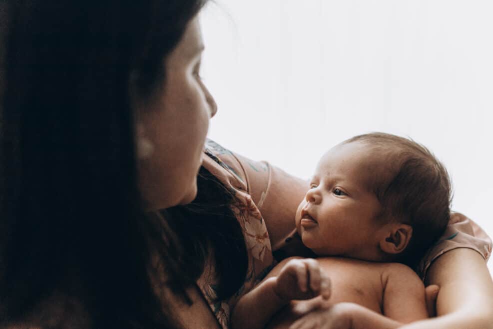 Happy Mothers day! Stylish Mother holding and hugging cute newborn baby in window light, close up. Motherhood and parenthood. Adoption and fertility concept