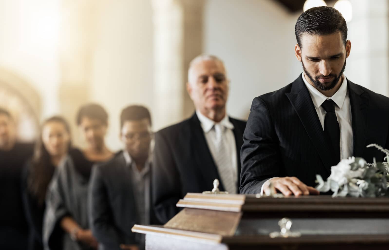 People, sad and funeral coffin, death and grief in church during ceremony or service, depression or floral. Support, emotional pain and sorry with casket, mourning and man in suit at casket in chapel