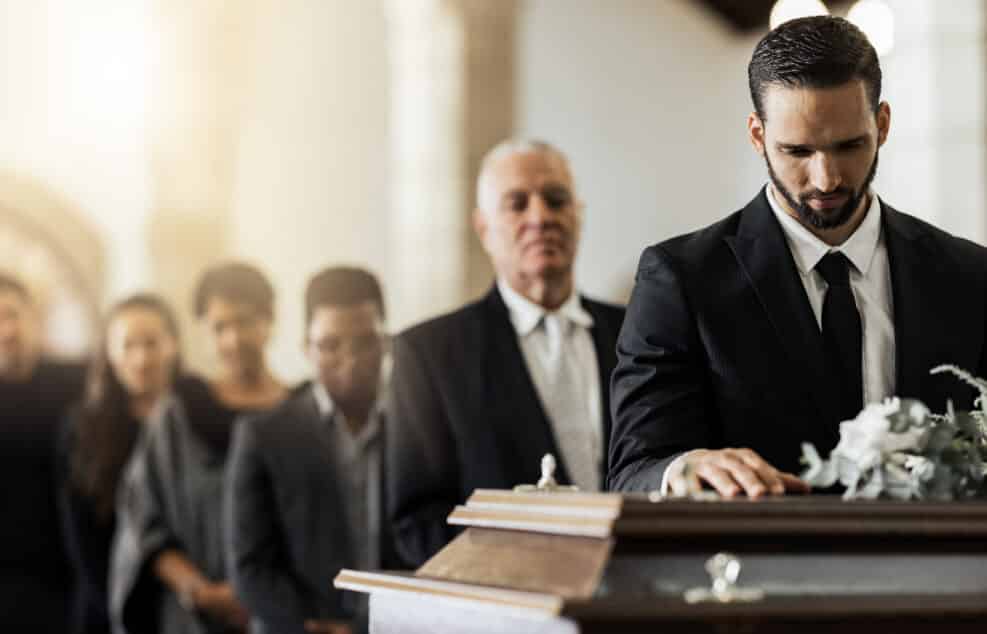 People, sad and funeral coffin, death and grief in church during ceremony or service, depression or floral. Support, emotional pain and sorry with casket, mourning and man in suit at casket in chapel
