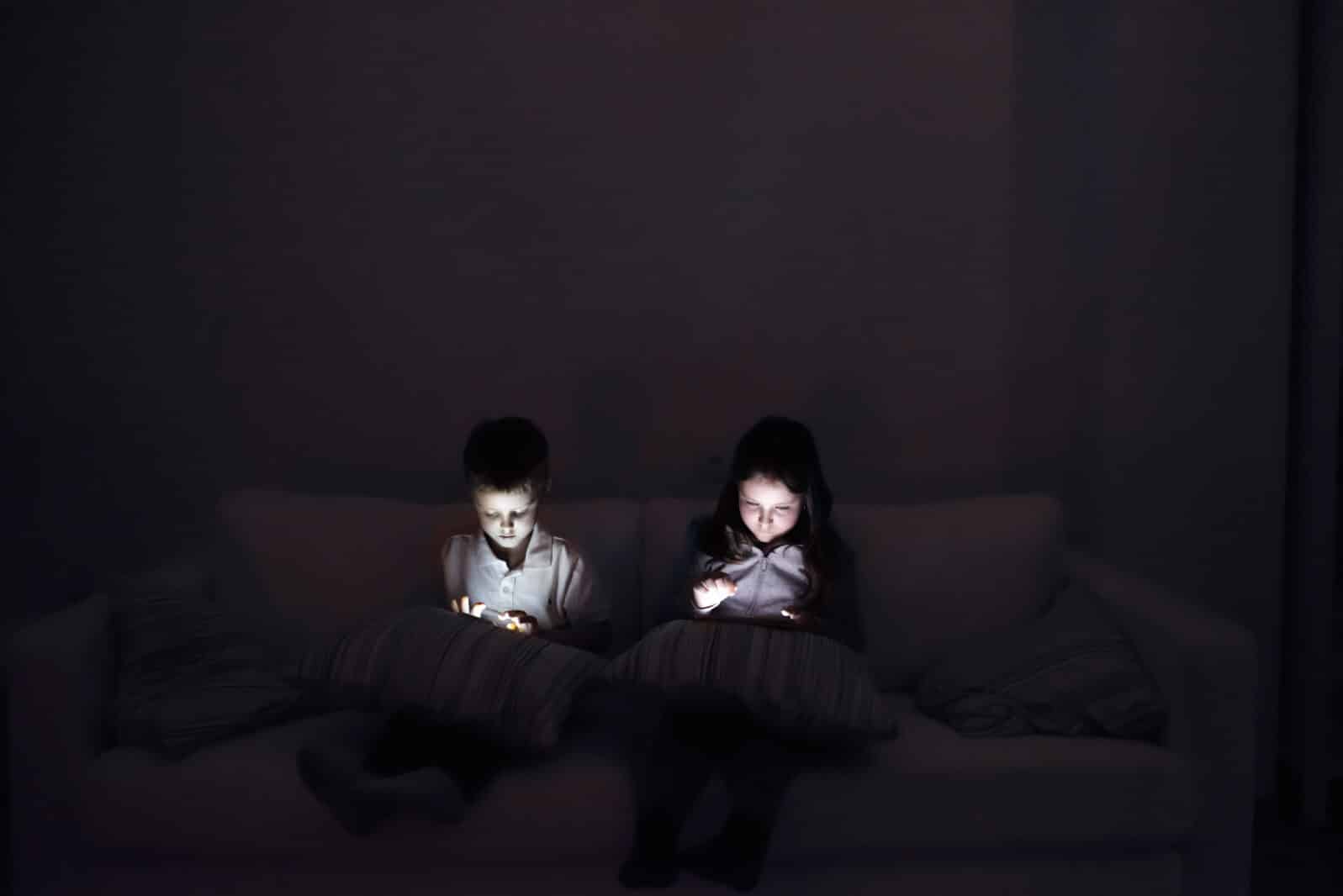 Two children, sitting in a dark, playing with gadgets