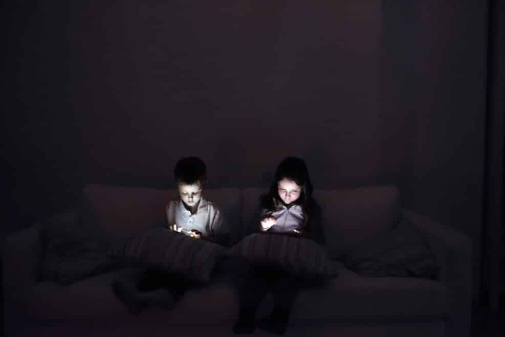 Two children, sitting in a dark, playing with gadgets